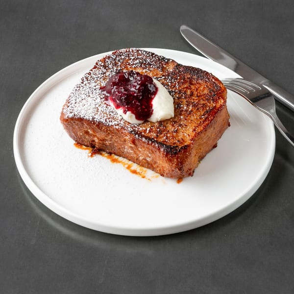Thick-cut French toast with powdered sugar, berry compote, and whipped cream on a white plate.