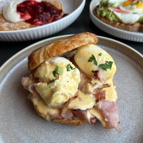 Croissant Eggs Benedict with ham, hollandaise, and chives, alongside other breakfast dishes.