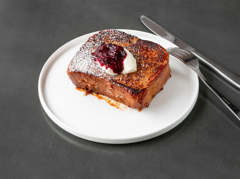 Thick-cut French toast with powdered sugar, whipped cream, and berry compote on a white plate.