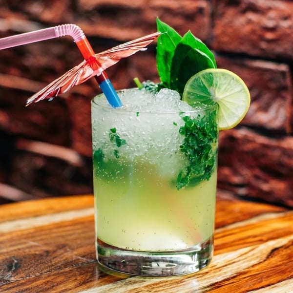 Refreshing mojito cocktail with crushed ice, mint, lime, and a decorative umbrella on a wooden table.