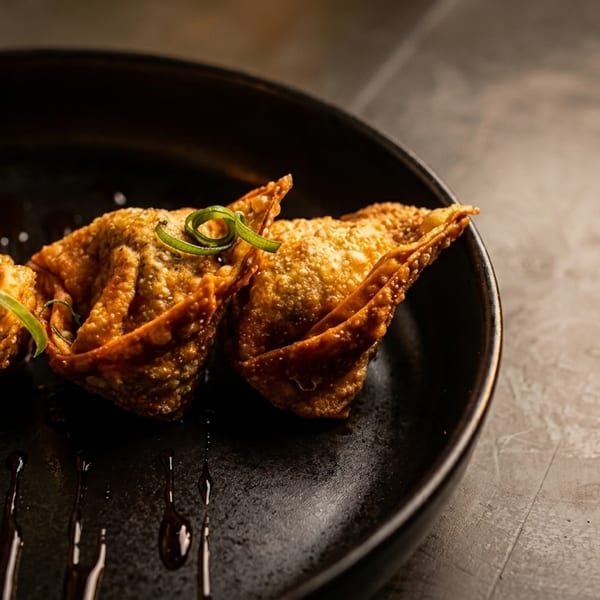 Crispy fried wontons garnished with green onions and a dark sauce on a black plate.